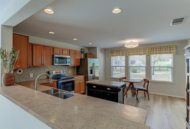 kitchen with brown cabinets, tasteful backsplash, visible vents, appliances with stainless steel finishes, and a sink