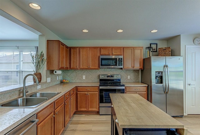 kitchen featuring light wood finished floors, appliances with stainless steel finishes, decorative backsplash, and a sink