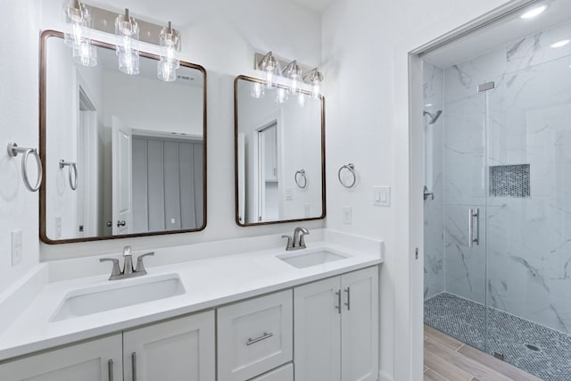 full bath with double vanity, a marble finish shower, a sink, and wood finished floors