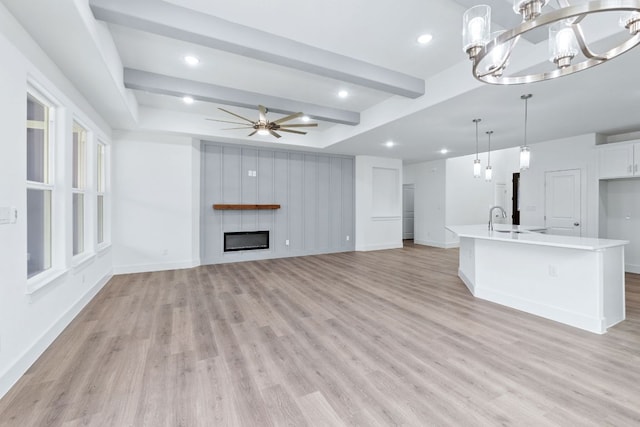 unfurnished living room with light wood-type flooring, a glass covered fireplace, baseboards, and ceiling fan with notable chandelier