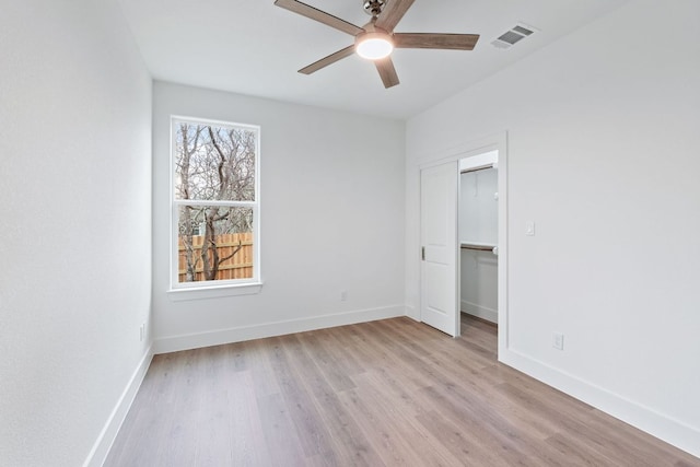 unfurnished bedroom with light wood finished floors, visible vents, a spacious closet, a ceiling fan, and baseboards