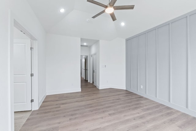 unfurnished room featuring light wood-type flooring, vaulted ceiling, a decorative wall, and ceiling fan