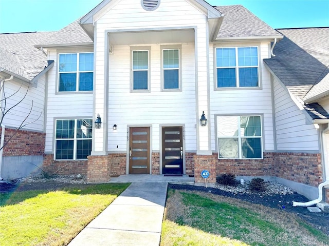 view of front of home with a shingled roof, a front yard, and brick siding