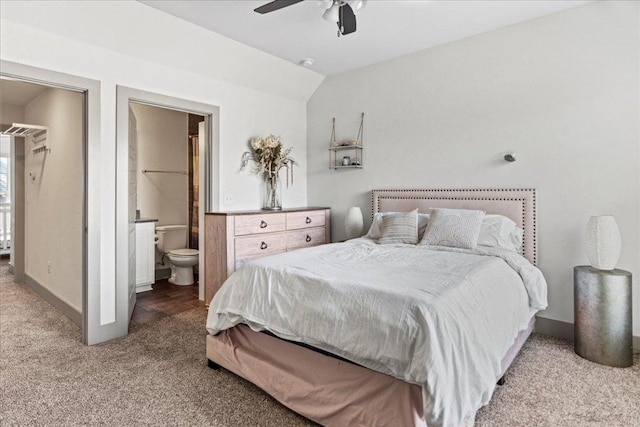 carpeted bedroom with ensuite bathroom, vaulted ceiling, baseboards, and a ceiling fan