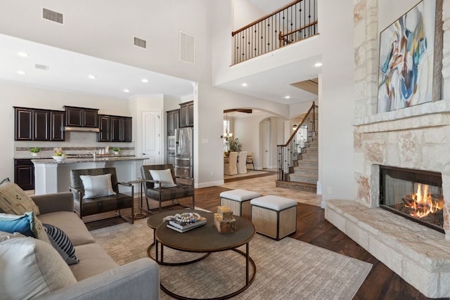 living area with visible vents, arched walkways, stairway, a stone fireplace, and light wood-style floors