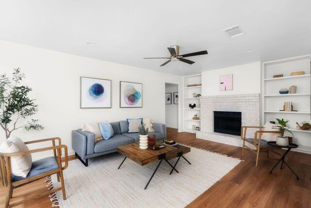 living room featuring visible vents, built in shelves, a ceiling fan, wood finished floors, and a fireplace