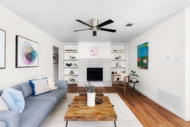 living room featuring built in features, wood finished floors, visible vents, and ceiling fan