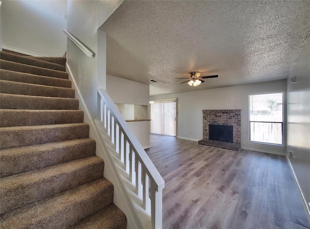 stairway featuring baseboards, a ceiling fan, wood finished floors, a textured ceiling, and a brick fireplace