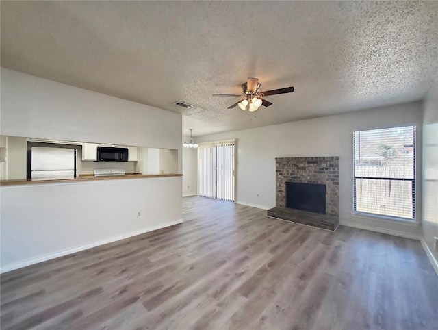 unfurnished living room featuring baseboards, wood finished floors, a textured ceiling, a brick fireplace, and ceiling fan with notable chandelier