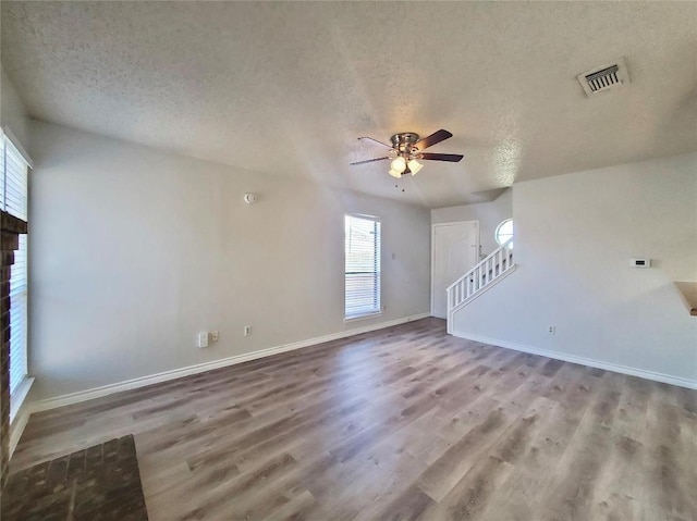 unfurnished living room featuring a textured ceiling, stairs, visible vents, and wood finished floors