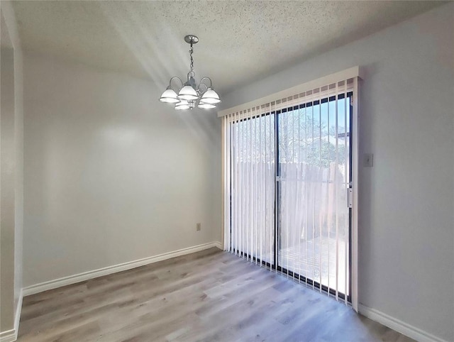 unfurnished room with a chandelier, a textured ceiling, wood finished floors, and baseboards