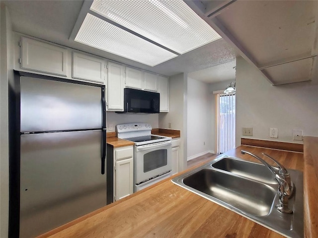 kitchen featuring white range with electric cooktop, butcher block counters, freestanding refrigerator, a sink, and black microwave