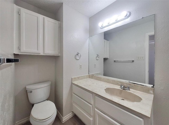 bathroom with baseboards, toilet, vanity, and a textured ceiling