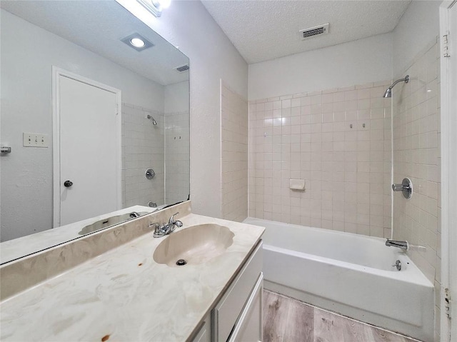 bathroom with a textured ceiling, wood finished floors, vanity, visible vents, and tub / shower combination