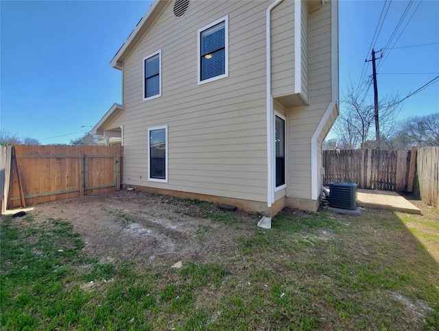 rear view of house with central AC, a lawn, and a fenced backyard