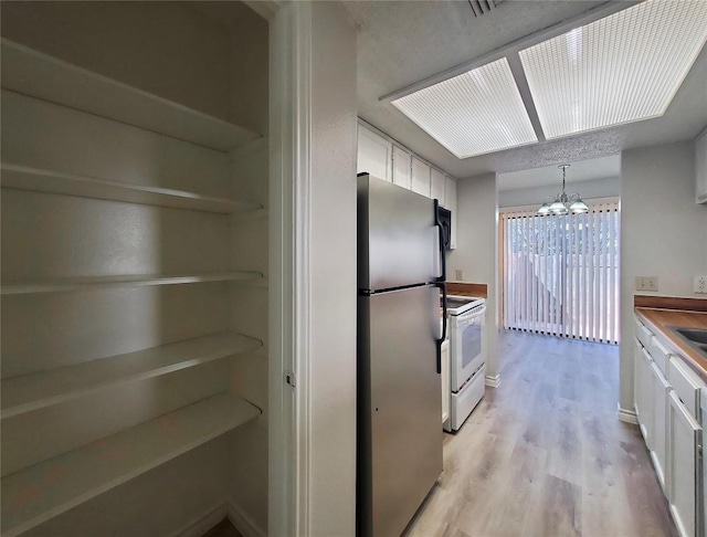 kitchen with white range with electric stovetop, a chandelier, white cabinets, and freestanding refrigerator