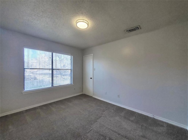 empty room with a textured ceiling, dark carpet, visible vents, and baseboards