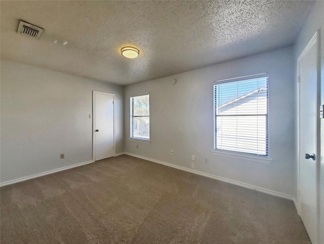 empty room with a textured ceiling, carpet flooring, visible vents, and baseboards