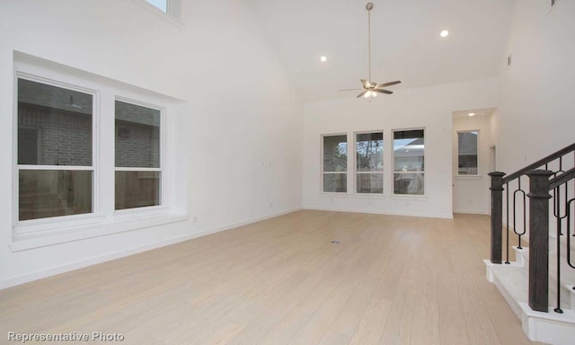 unfurnished living room featuring light wood finished floors, baseboards, ceiling fan, stairs, and high vaulted ceiling