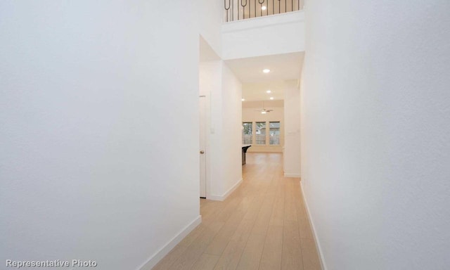 corridor with light wood-type flooring, a high ceiling, and baseboards