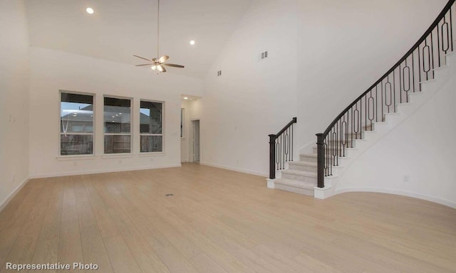 unfurnished living room with hardwood / wood-style floors, a high ceiling, a ceiling fan, baseboards, and stairs