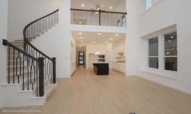 unfurnished living room featuring light wood finished floors, baseboards, a towering ceiling, stairway, and recessed lighting