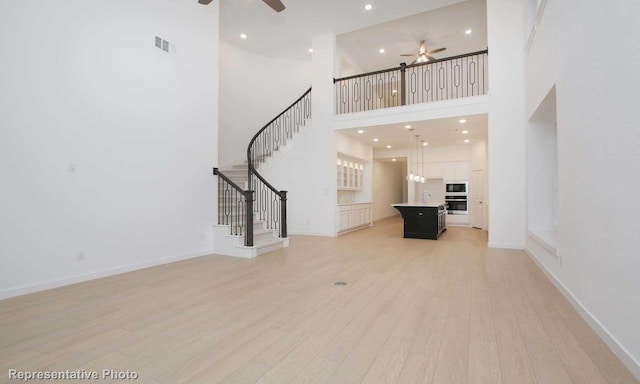 unfurnished living room with light wood-type flooring, ceiling fan, visible vents, and stairway