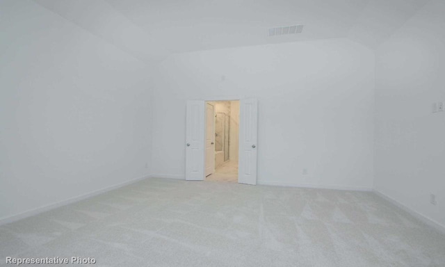 spare room featuring light carpet, baseboards, lofted ceiling, and visible vents
