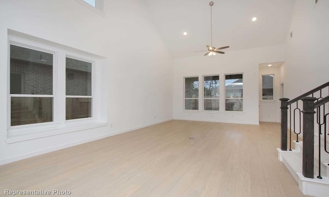 unfurnished living room featuring light wood-type flooring, baseboards, stairs, ceiling fan, and high vaulted ceiling