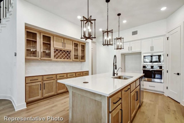 kitchen featuring light wood finished floors, built in microwave, a sink, and stainless steel oven