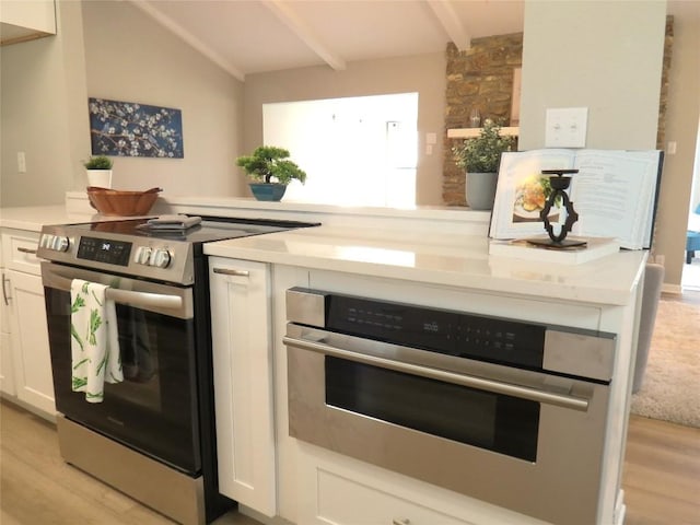 kitchen with appliances with stainless steel finishes, white cabinetry, light wood-style floors, and lofted ceiling with beams