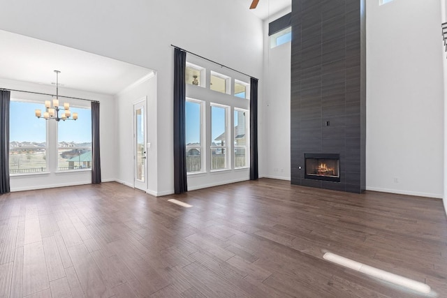 unfurnished living room featuring a towering ceiling, a fireplace, dark wood finished floors, and ceiling fan with notable chandelier