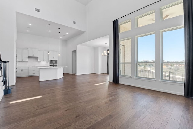 unfurnished living room featuring baseboards, visible vents, a towering ceiling, dark wood-style floors, and a chandelier