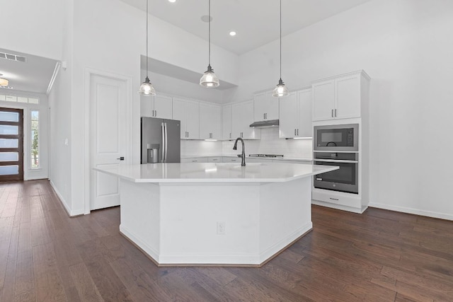 kitchen featuring tasteful backsplash, appliances with stainless steel finishes, dark wood-type flooring, light countertops, and under cabinet range hood