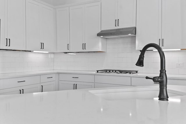 kitchen with under cabinet range hood, white cabinetry, light countertops, and decorative backsplash