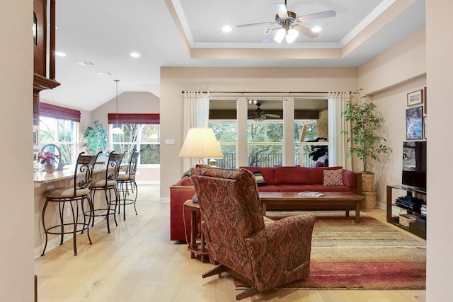 living room featuring light wood-style flooring, a tray ceiling, ceiling fan, and ornamental molding