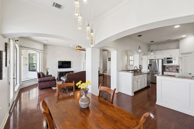 dining area with arched walkways, a fireplace, dark wood finished floors, and visible vents