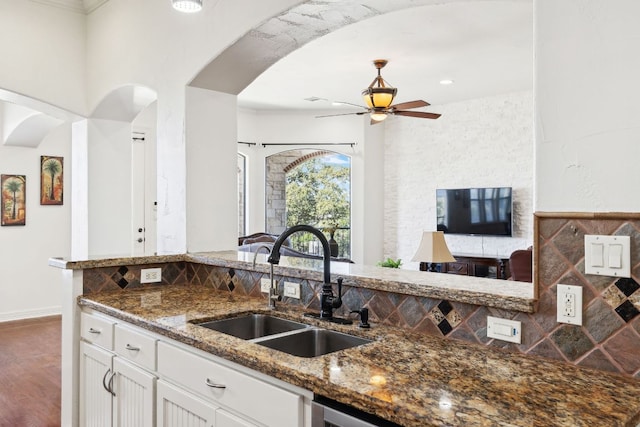 kitchen with arched walkways, a sink, white cabinets, decorative backsplash, and dark stone counters