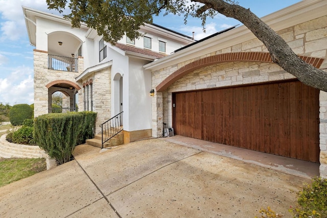 mediterranean / spanish home featuring a garage, concrete driveway, a balcony, stone siding, and stucco siding