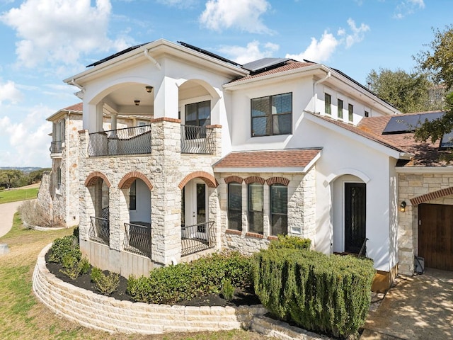 mediterranean / spanish-style house featuring stone siding, roof mounted solar panels, a balcony, and stucco siding