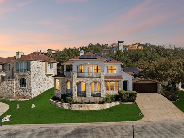 view of front of property featuring a balcony, an outdoor structure, a yard, concrete driveway, and roof mounted solar panels