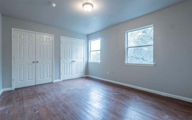 unfurnished bedroom with multiple windows, two closets, baseboards, and wood finished floors