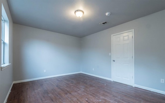 empty room with dark wood finished floors, baseboards, and visible vents