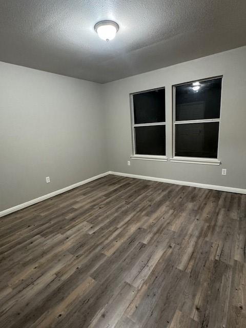 unfurnished room featuring dark wood-type flooring, baseboards, and a textured ceiling