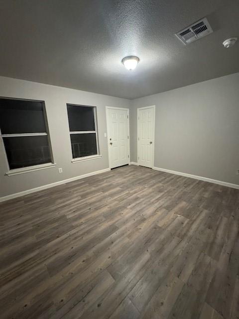 empty room featuring dark wood finished floors, visible vents, a textured ceiling, and baseboards