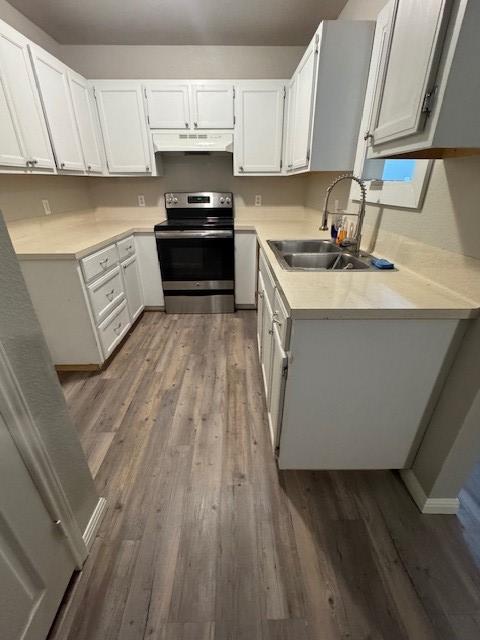 kitchen featuring under cabinet range hood, light countertops, stainless steel range with electric cooktop, wood finished floors, and a sink