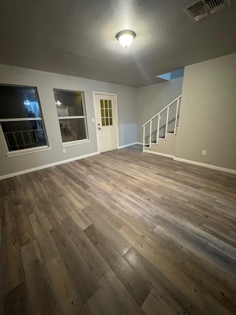 unfurnished living room with a textured ceiling, visible vents, dark wood-type flooring, and stairway