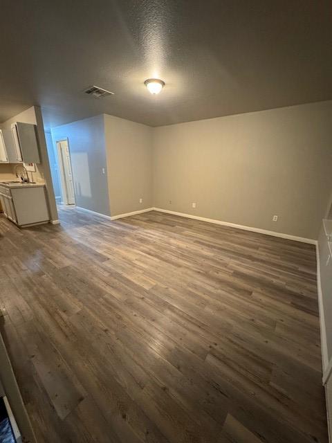 unfurnished room with visible vents, baseboards, a textured ceiling, and dark wood-style flooring