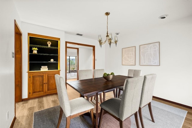 dining room featuring light wood finished floors, baseboards, visible vents, built in features, and a chandelier