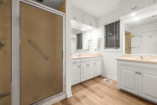 full bathroom with a shower stall, baseboards, two vanities, and wood finished floors